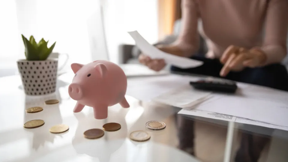 Mealheiro com moedas e pessoa a analisar despesas, representando os custos do crédito habitação.