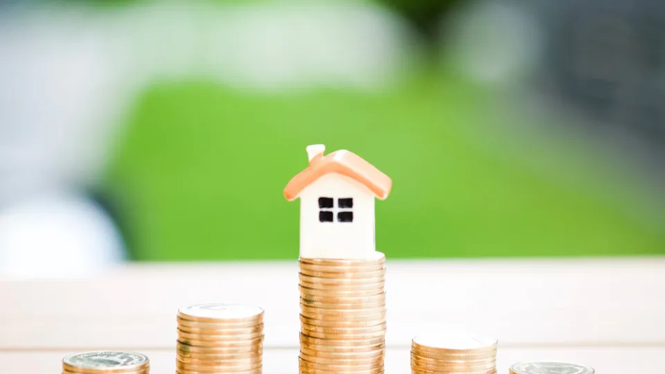 Maquete de uma casa sobre pilhas de moedas, representando a compra de um imóvel penhorado