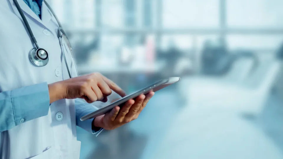 Profissional de saúde a utilizar um tablet, simbolizando a comparação entre seguro de saúde, plano de saúde e cartão de saúde.