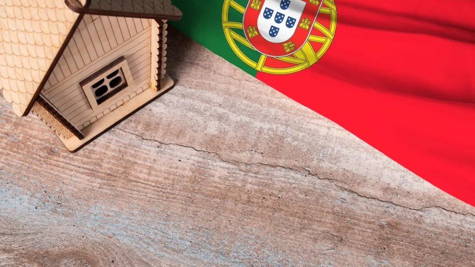 Maquete de uma casa junto à bandeira de Portugal, simbolizando o crédito habitação para emigrantes portugueses.