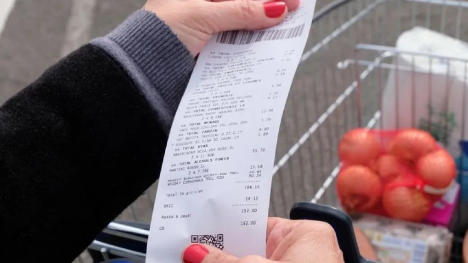Pessoa a analisar o talão de compras ao lado de um carrinho de supermercado, simbolizando o controlo de gastos e a poupança nas compras.