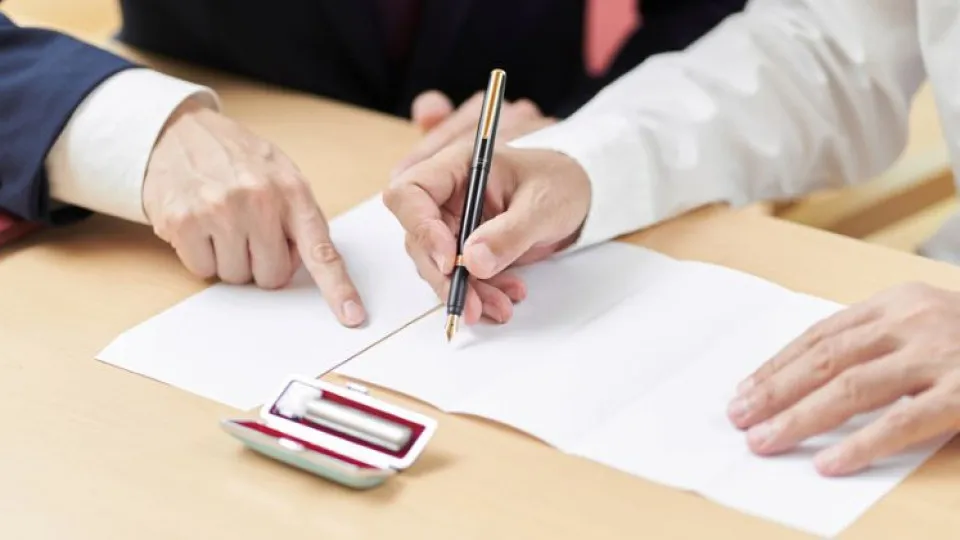Mãos de mulher a assinar contrato de crédito com dedo indicador de homem a apontar para a folha 