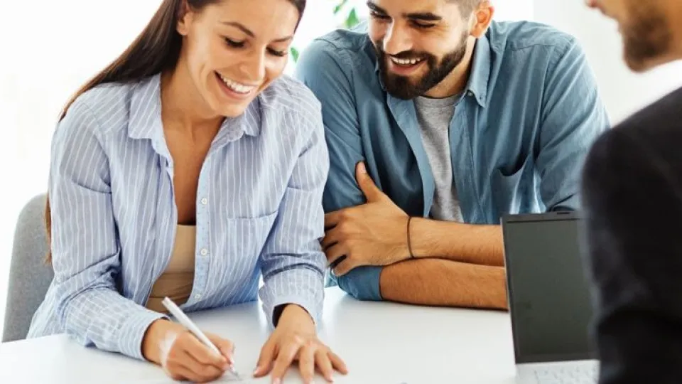 Casal feliz sentados a assinar contrato de crédito habitação em mesa 
