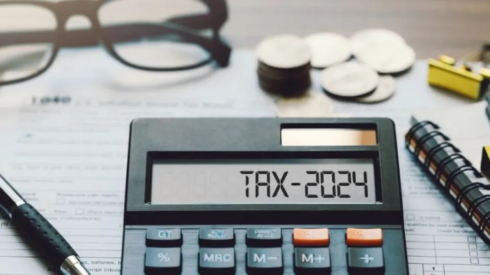 Calculadora com tax 2024, IMI, caneta, caderno, óculos, clips e moedas em cima de folhas sob mesa