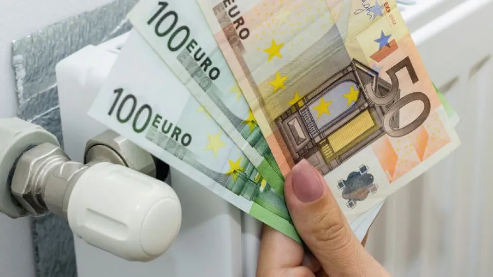 Aquecedor a gás e mulher com mão à frente a exibir notas de 50 e 100 euros 