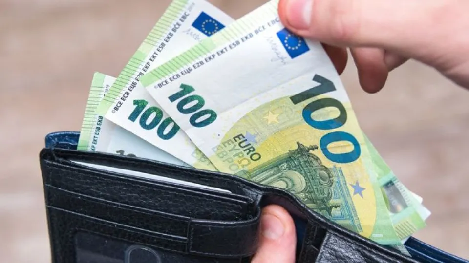 Carteira em mãos a retirar notas de 100 euros simbolizando prestação de maio