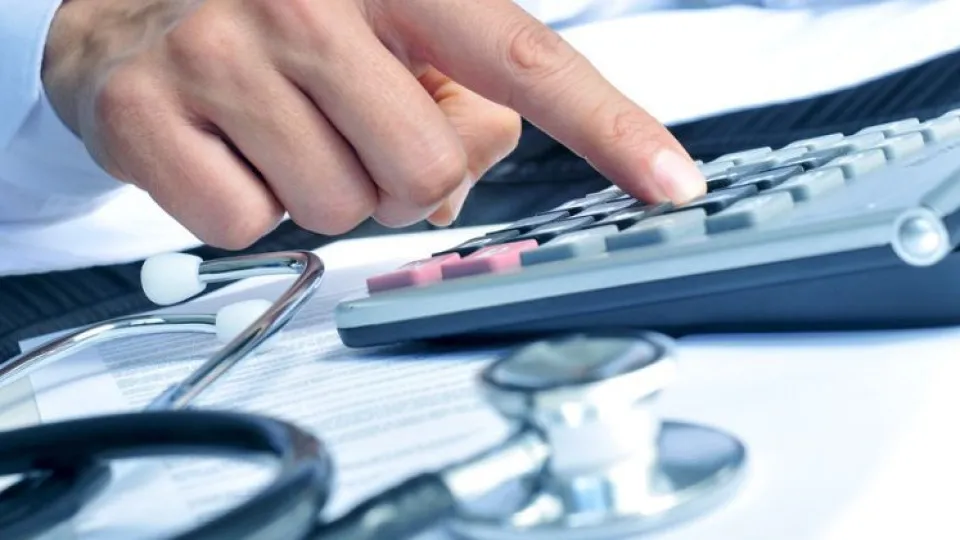 Mão a carregar em calculadora e estetoscópio do lado simbolizando custos em empresas