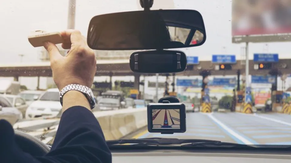 Mão de pessoa dentro de carro a ajustar aparelho de portagens em estrada antes das portagens