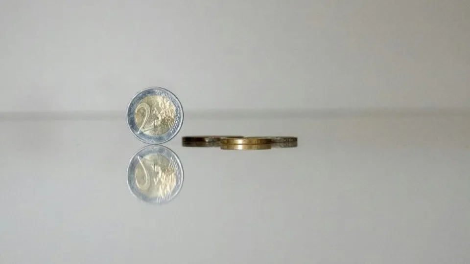 Moeda de dois euros em pé e moedas deitadas para simbolizar poupar dinheiro