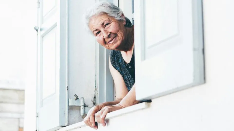 Senhora idosa à janela simbolizando apoios