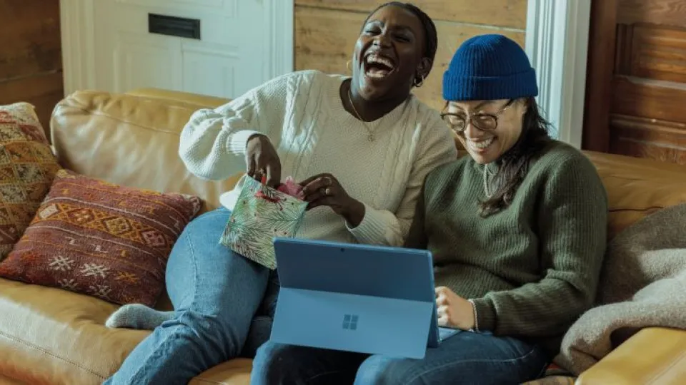 Casal jovem sentado em sofá com computador à frente e a sorrir simbolizando compra de casa por jovens com financiamento a 100% e isenções fiscais