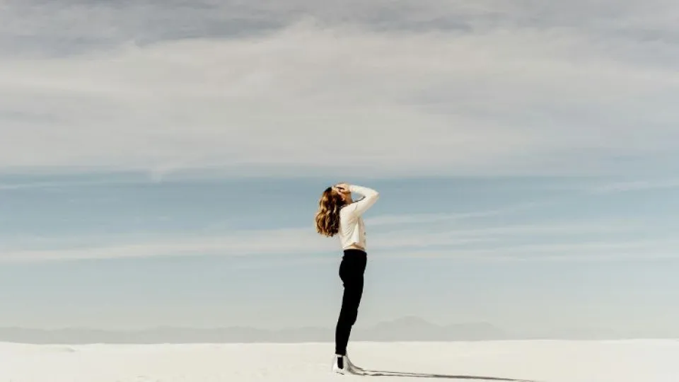 Mulher em areia com mãos na cabeça para simbolizar frustração da subida de taxas de juros