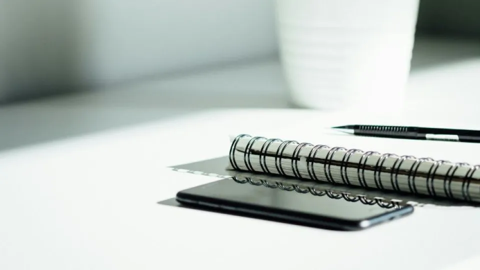 Telemóvel, caderno e caneta em mesa branca simbolizando nota de cobrança do IMI