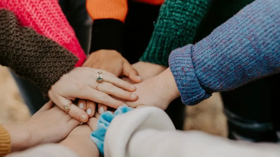 Grupo de pessoas com as mãos unidas, simbolizando união e apoio - conceito de juntar créditos num só para simplificar e poupar.