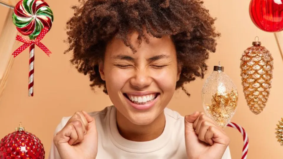 Pessoa a sorrir com entusiasmo rodeada de decorações natalícias, representando a expectativa positiva de receber o subsídio de Natal.