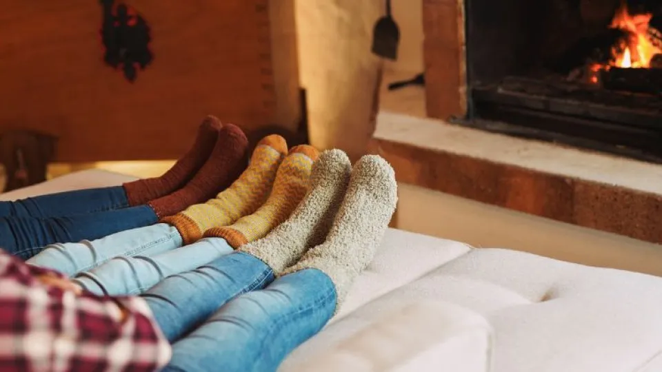 Pessoas de meias sentadas junto à lareira, simbolizando conforto e técnicas rápidas para aquecer uma divisão da casa.
