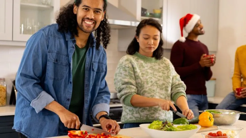 Grupo de amigos a preparar comida numa cozinha, simbolizando celebrações sustentáveis e partilha consciente.