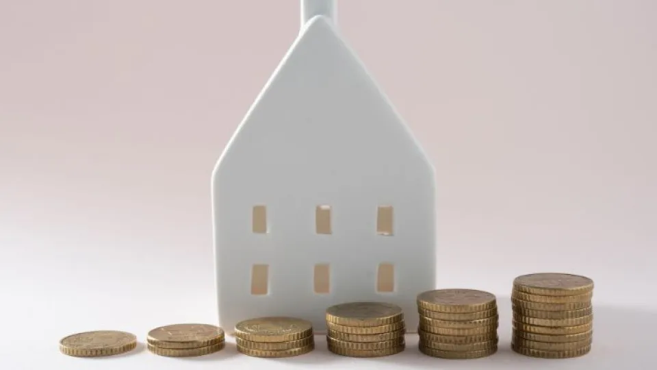 Casa branca em miniatura com pilhas de moedas alinhadas em crescimento - conceito de crédito habitação, investimento ou valorização do imóvel.
