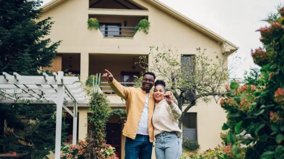 Casal a sorrir no jardim enquanto olha para a casa nova, simbolizando a decisão de investir num crédito habitação no início do ano.