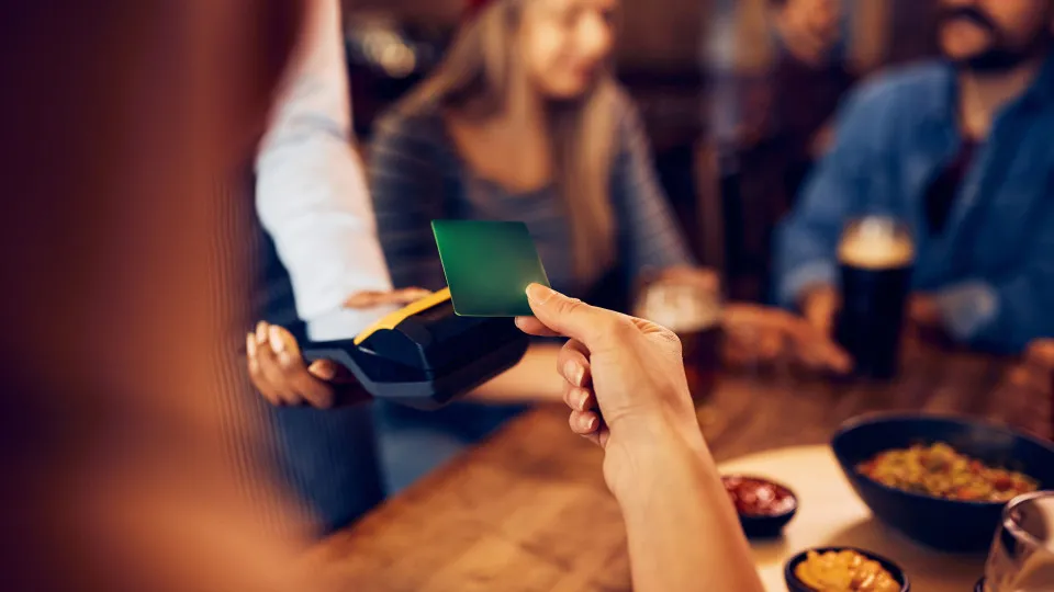Pessoa a pagar com cartão num restaurante, enquanto janta com amigos.