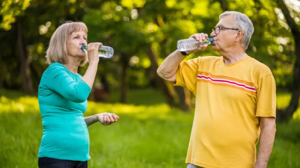 Casal sénior a beber água num parque, promovendo hábitos saudáveis para uma vida mais longa