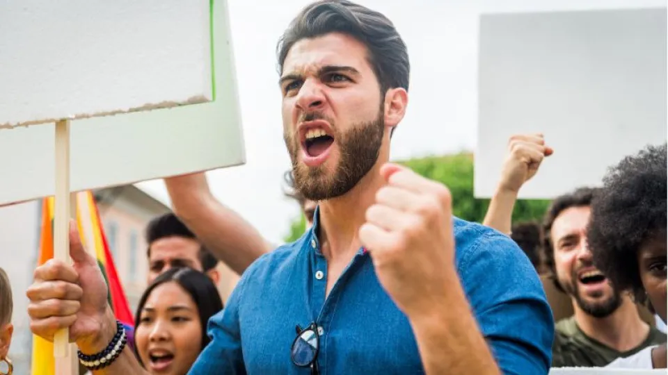 Homem com placa na mão e pessoas atrás a contestar em grupo fazendo greve