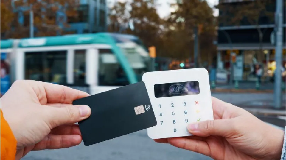Cartão a fazer pagamento eletrónico em máquina branca num fundo de rua com um autocarro
