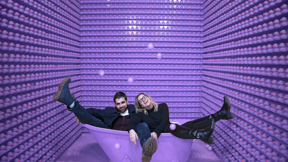 Casal jovem descontraído dentro de uma banheira decorativa, num cenário criativo, simbolizando liberdade e leveza após conseguir crédito habitação 100% financiado.