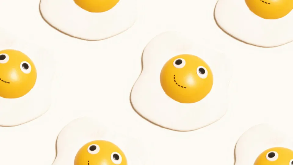 Gemas de ovo com olhos e sorriso desenhados, dispostas num fundo branco, criando um padrão divertido e alegre.