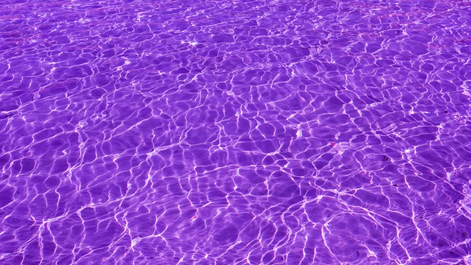Superfície de água ondulada em tons de roxo, com reflexos de luz, evocando um ambiente relaxante e estival.