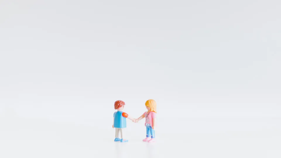 Miniaturas de um casal de mãos dadas, representando união de facto ou relação amorosa, sobre fundo branco minimalista.