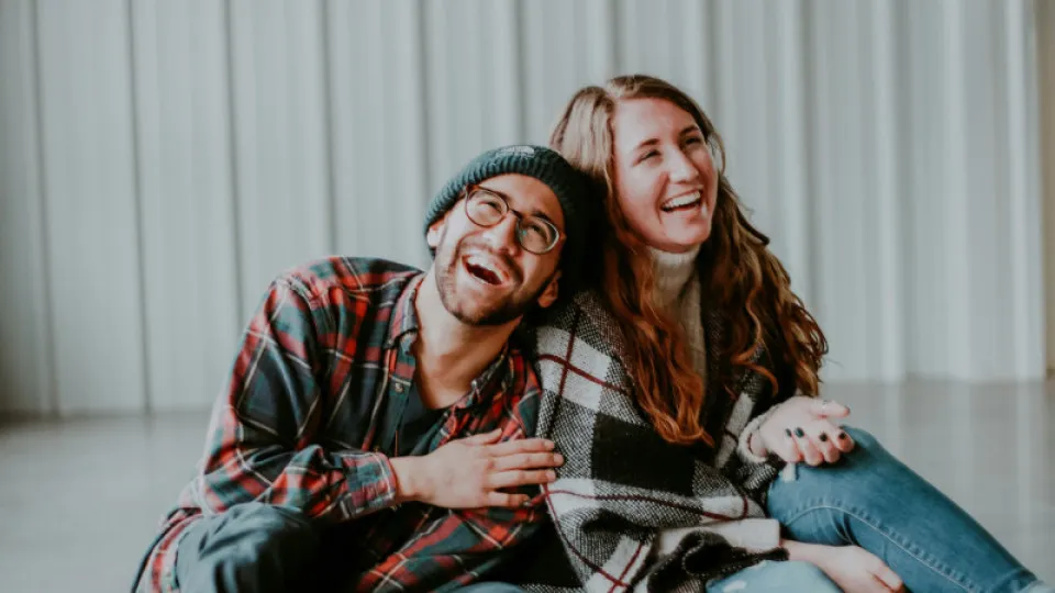 Casal jovem e feliz sentado no chão, a rir descontraidamente, simbolizando cumplicidade e bem-estar numa relação de união de facto.