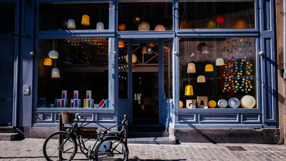 Loja com fachada envidraçada e candeeiros pendurados no interior, vista da rua com bicicleta estacionada em frente.