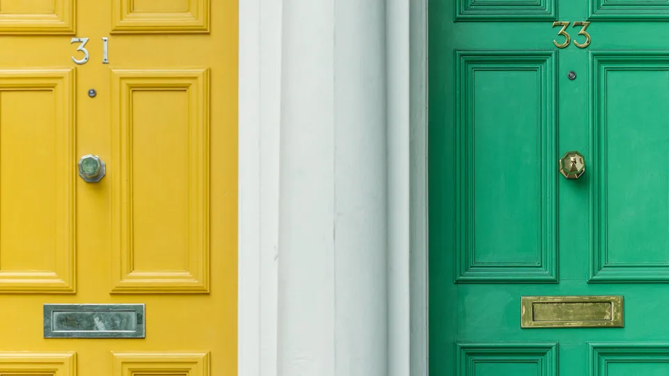 Duas portas lado a lado – uma amarela e outra verde – simbolizando duas casas. A imagem representa o conceito de contratar um segundo crédito habitação.