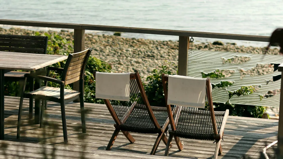 Terraço com espreguiçadeiras e mesa de madeira voltado para o mar.