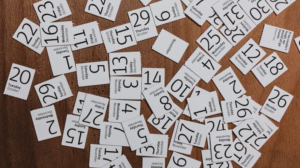 Folhas de calendário com diferentes dias e meses espalhadas sobre uma mesa.