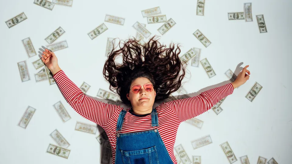 Pessoa deitada no chão rodeada de notas, simbolizando liberdade financeira alcançada através de hábitos de poupança.