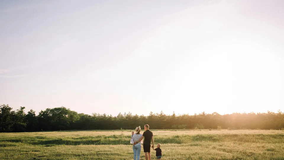 Família a caminhar num campo ao pôr do sol, simbolizando estabilidade e equilíbrio alcançados através de uma boa gestão do orçamento familiar.
