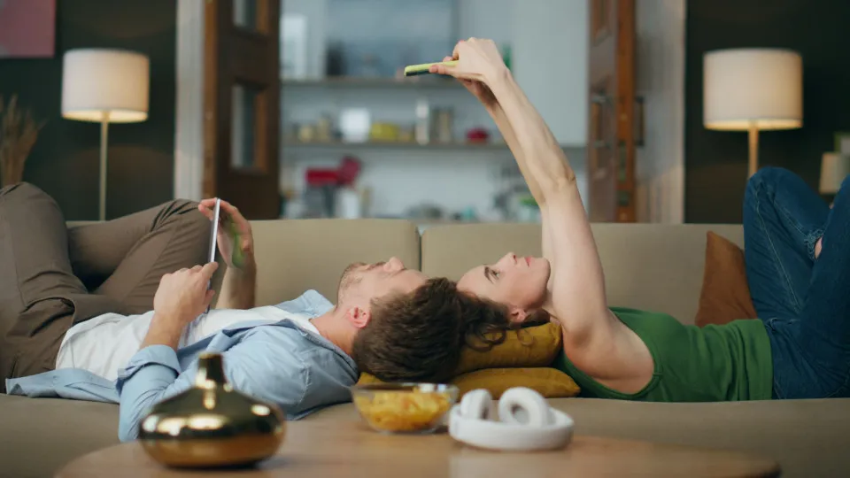 Casal relaxado no sofá a ver o telemóvel, simbolizando tranquilidade após encontrar soluções para reduzir a prestação do crédito habitação.