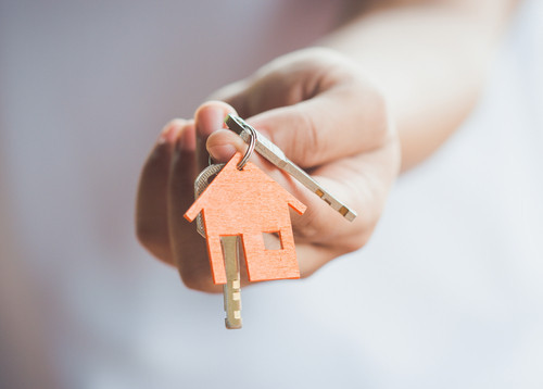 Uma mão a segurar chaves com um porta-chaves com uma casa que visa representar o ato de comprar casa